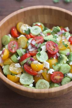 a wooden bowl filled with cucumber, tomato and feta cheese salad on top of a table