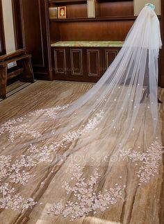 the bride is wearing a long veil with flowers on it and she is looking down at her wedding dress