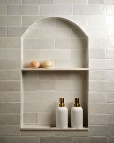 two bottles are sitting on a shelf in front of a white brick wall with an arched niche