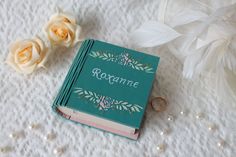 an open book sitting on top of a table next to two white flowers and pearls