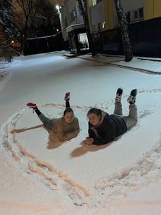 two people laying in the snow making a heart