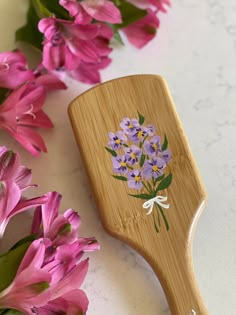 a wooden spatula with flowers painted on it next to pink and purple tulips