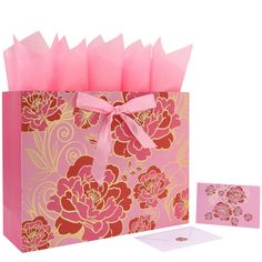 a pink and gold gift bag with flowers on it, next to a greeting card