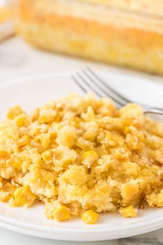 a white plate topped with corn casserole next to a fork and glass container