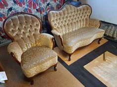 two gold chairs sitting next to each other on top of a hard wood floor in front of a floral wallpaper