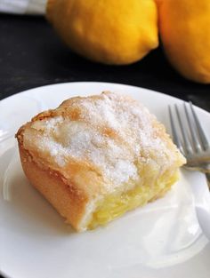 a white plate topped with a piece of cake and two lemons in the background