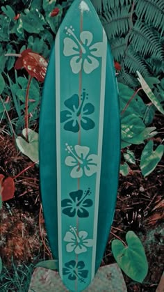 a blue surfboard sitting on top of a rock in front of some plants and leaves