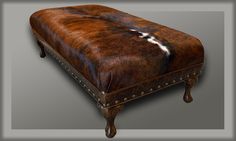 a brown leather ottoman with white and black fur on the top, sitting in front of a gray background