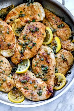 chicken with lemons and capers in a skillet on a marble countertop