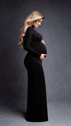 a pregnant woman in a long black dress poses for a photo with her hands on her belly