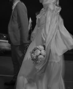 a bride and groom walking down the street at night in black and white, dressed up for their wedding