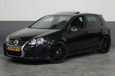 a black car parked in a garage next to a white wall and grey flooring