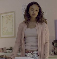 a woman standing in front of a bed wearing a pink cardigan