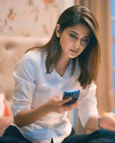 a woman sitting on a bed looking at her cell phone while holding it in her hand