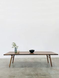 a wooden table with two black bowls on it and a plant in the middle, against a white wall