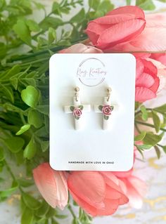 two white earrings with pink flowers in the background on a card and some green leaves