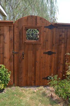 a wooden gate with a window in the middle and green bushes around it on either side