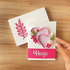 someone is holding up two cards with hearts and flowers on them, one has the word hugs