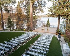 an outdoor ceremony set up with white chairs and flowers on the lawn, overlooking a lake