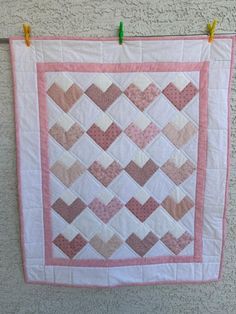 a pink and white quilt hanging on a wall with clothes pins in front of it