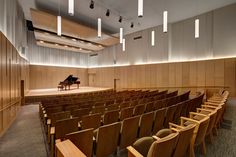 an auditorium with rows of chairs and a grand piano in the center is lit by recessed lights