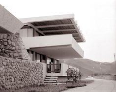 a black and white photo of a building with rocks on the outside, and grass in front