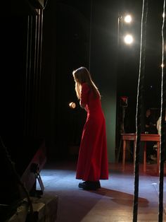 a woman in a red dress is standing on the stage with her hands behind her back