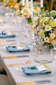 a long table is set with blue and yellow napkins, silverware, and flowers