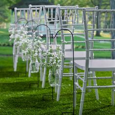 rows of white chairs with flowers in vases lined up on the grass near each other