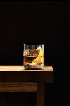 a glass filled with liquid sitting on top of a wooden table next to a slice of lemon