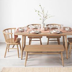 a wooden table with chairs and plates on it in front of a white painted wall