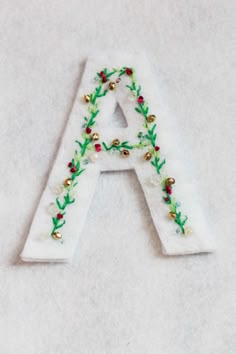 a white letter decorated with green and red beads on it's side, sitting on a table