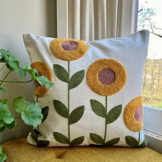 a pillow with yellow flowers on it sitting next to a potted plant in front of a window