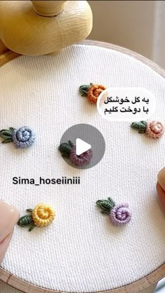 someone is making crochet flowers on a piece of white fabric with words written in arabic