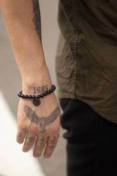 a man with a tattoo on his arm holding onto a beaded bracelet that has an eagle on it