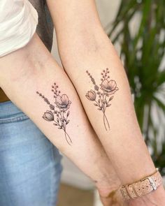 two women with matching tattoos on their arms holding each other's hands and flowers