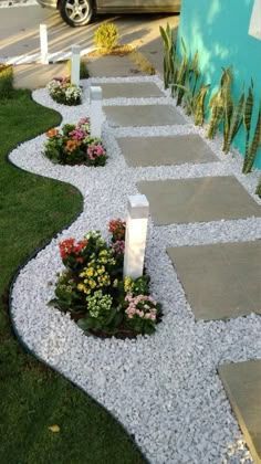 a walkway made out of stones and gravel with flowers in the middle next to it