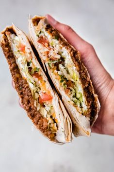 a hand holding two tacos filled with meat, cheese and veggie toppings