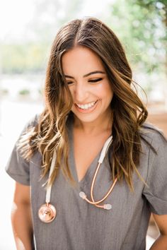 a woman wearing a gray shirt and stethoscope smiling at the camera with her hands on her hips