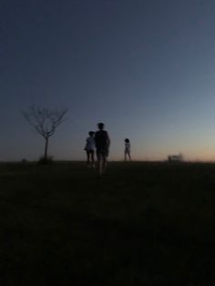 three people standing in a field at night with the sun setting behind them and one person flying a kite