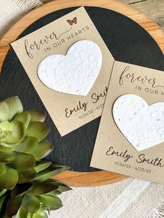 two heart shaped paper tags sitting on top of a wooden plate next to a succulent