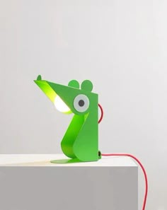 a green lamp sitting on top of a white table next to a red cord with an eye