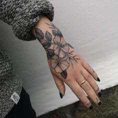 a woman's hand with black and white flowers tattooed on the left side of her arm