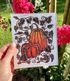 a hand holding up a card with an image of a pumpkin and flowers in the background