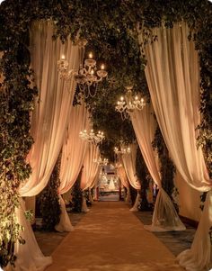 an outdoor ceremony with white drapes and chandeliers hanging from the ceiling, decorated with greenery