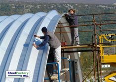 two men working on the side of a large metal structure with mountains in the background