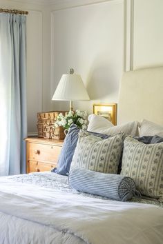 a bed with blue and white pillows on top of it next to a dresser in a bedroom