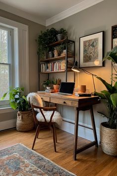 a desk with a laptop on it in front of a window and potted plants