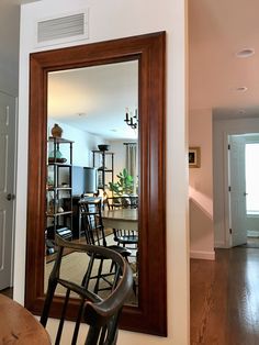 a large mirror in the middle of a room with chairs around it and a door leading to another room