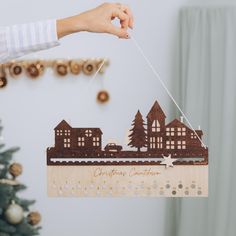 a wooden christmas ornament hanging on a string with a hand holding the string